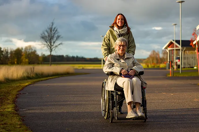 En person som kör en annan person i rullstol utomhus. 