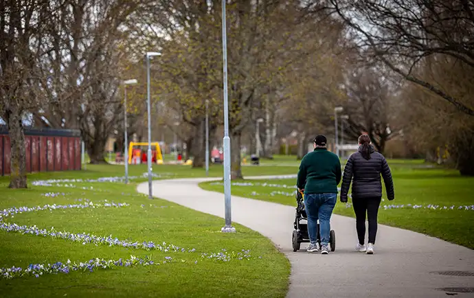 Par med barnvagn som går i en park