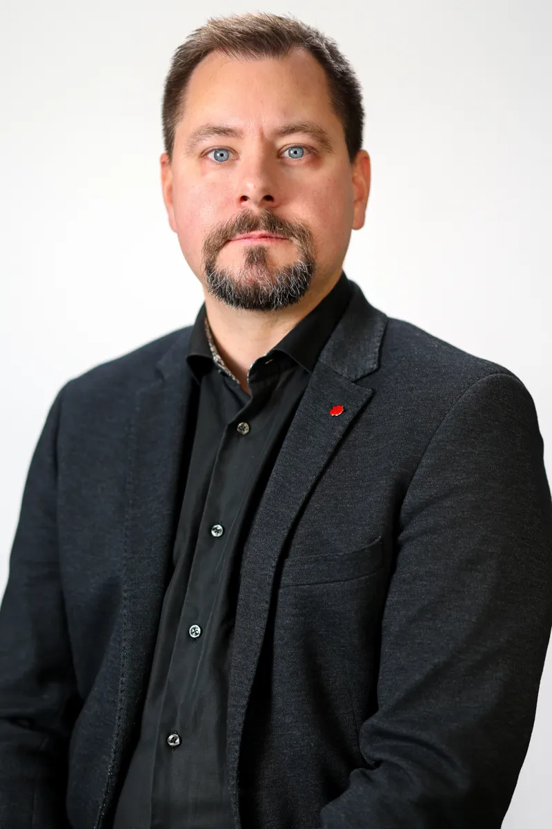 En man med skägg och svart skjorta.