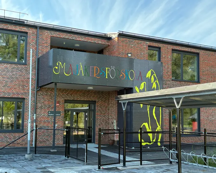 Majåkers röda träbyggnad och på gräset under flaggan sitter barn