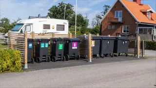 Bilden visar sju olika avfallskärl placerad i en kärlhage vid ett flerbostadshus.