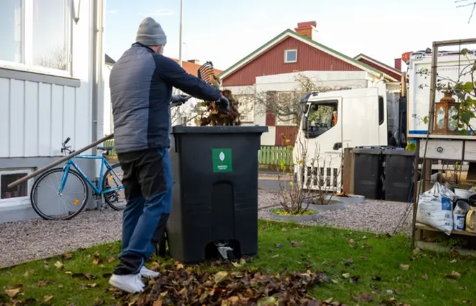 En man som fyller sitt kärl för trädgårdsavfall med höstlöv